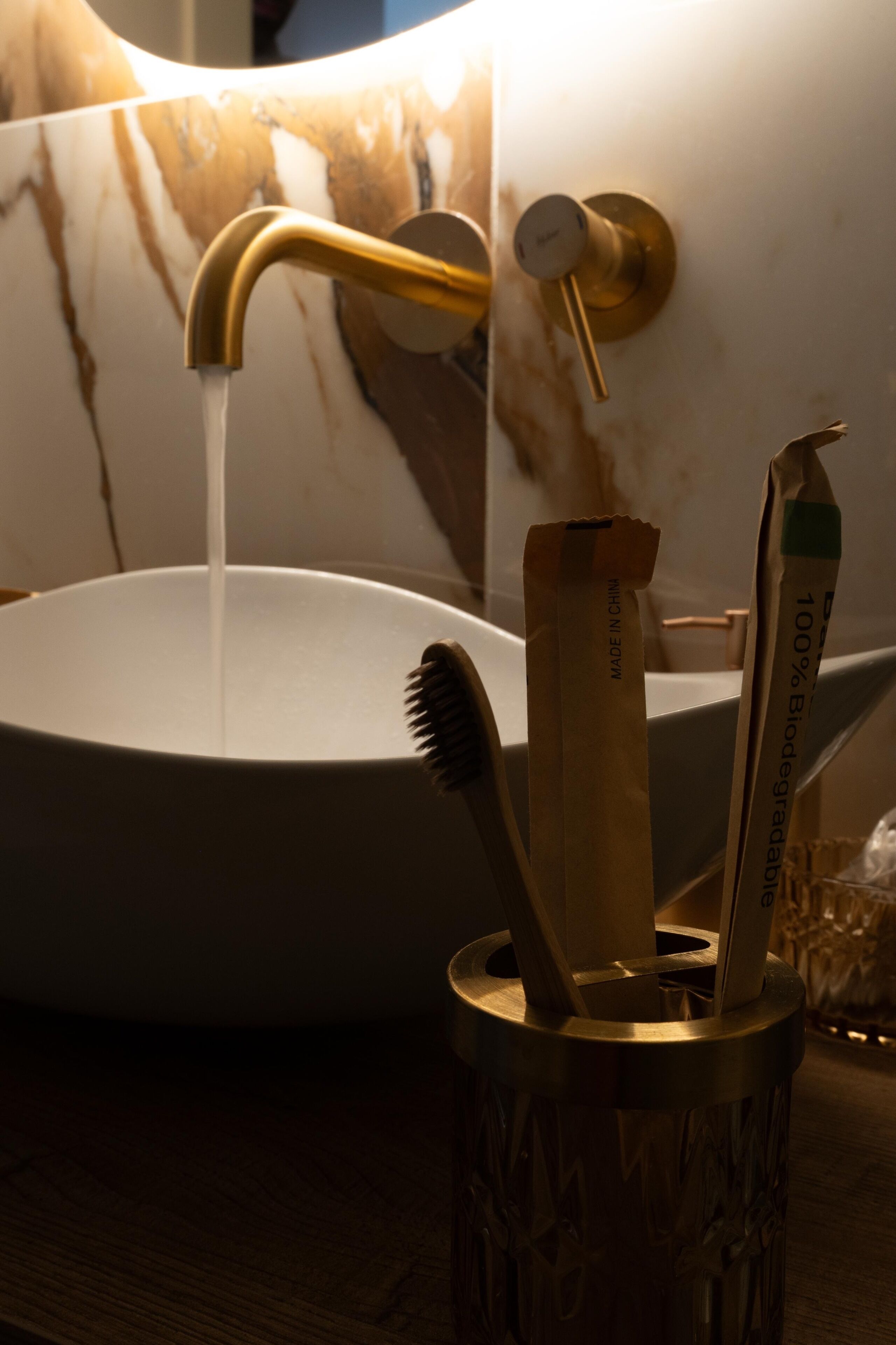 Ein Waschbecken mit goldfarbenem Wasserhahn, ein Zahnbürstenhalter mit Zahnbürste sowie eine Shampoo-Flasche.