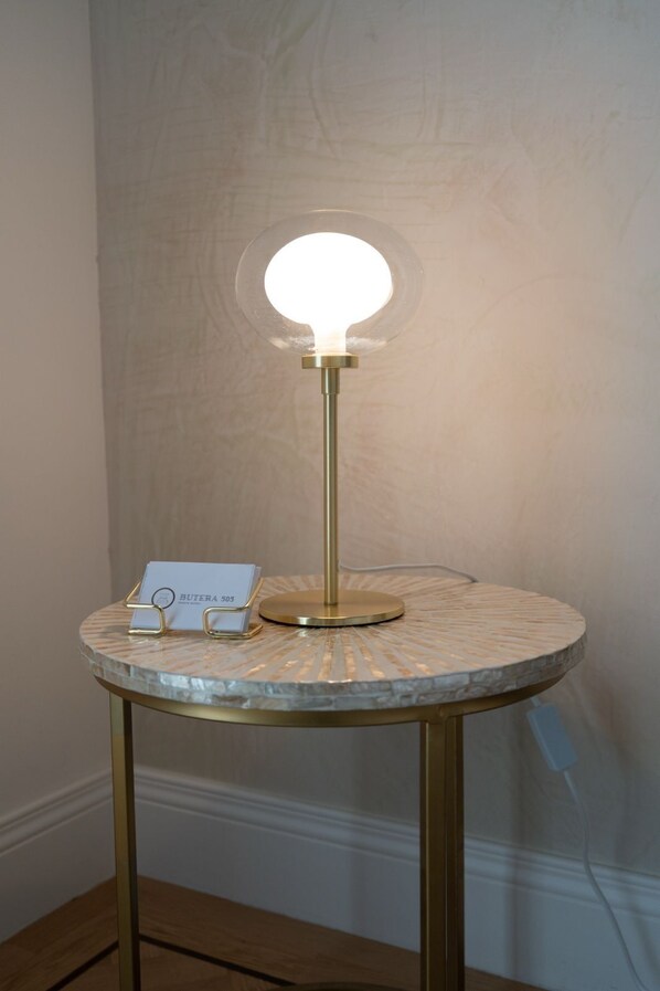 A table lamp with a round base and a clear glass shade, placed on a round table with a textured surface. - Butera505luxurysuites (Bagheria)