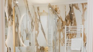 A modern bathroom with a glass-enclosed shower, a white sink, and marble-patterned walls. - Butera505luxurysuites (Bagheria)