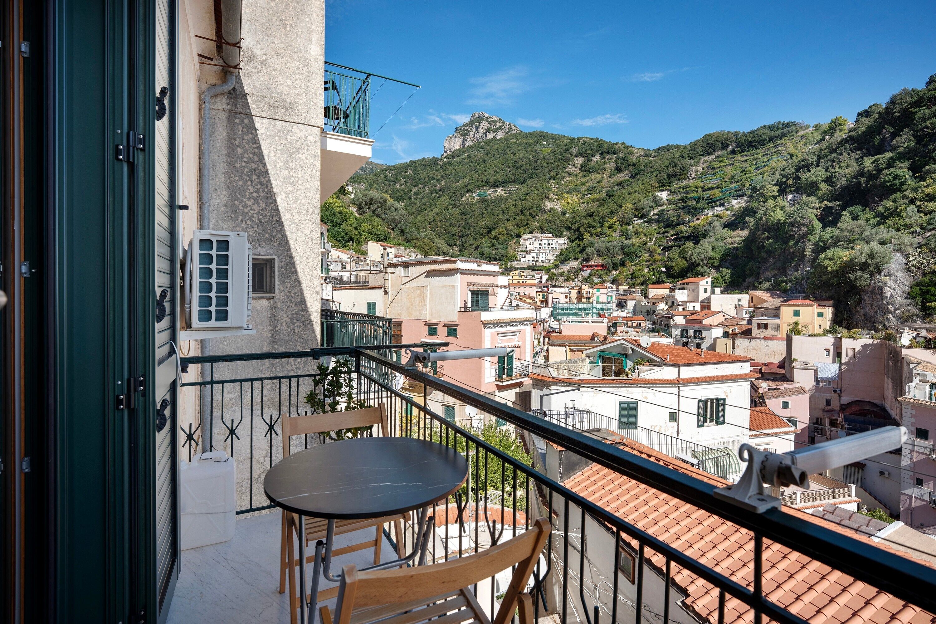 Un balcón con una mesa y sillas, con vista a un pueblo con edificios y una montaña.