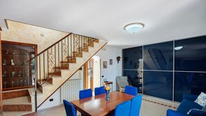 A dining area with a wooden table and blue chairs, a staircase with a railing, and a large window with a view of the outside. - Holiday Home 'A' Russella' with Sea View, Wi-Fi and Air Conditioning (Cetara)