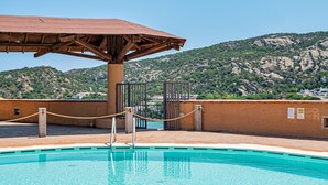 Una piscina con una pérgola de madera, una barrera de cuerda y un paisaje montañoso de fondo.