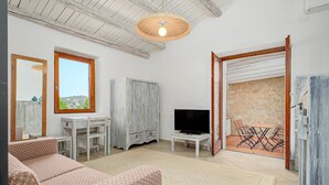 Una sala de estar con un sofá, televisión y vistas a un patio a través de una puerta abierta.