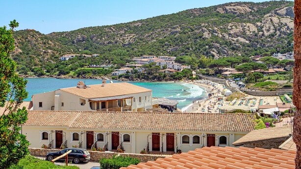 Un pueblo costero con edificios, una playa y montañas al fondo.