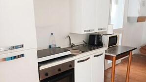 Eine kompakte Küche mit weißen Schränken, einem schwarzen Backofen, einer Spüle, einer Mikrowelle und einem kleinen Tisch.