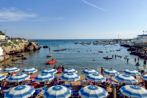 A coastal beach scene with umbrellas, boats, and people.