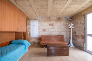Une pièce comprenant un lit, un canapé, une commode, une porte blanche et un mur en pierre.
