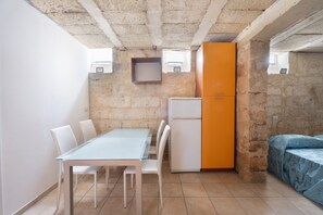 Une cuisine compacte avec une table en verre, des chaises blanches, un réfrigérateur blanc et un lit bleu.