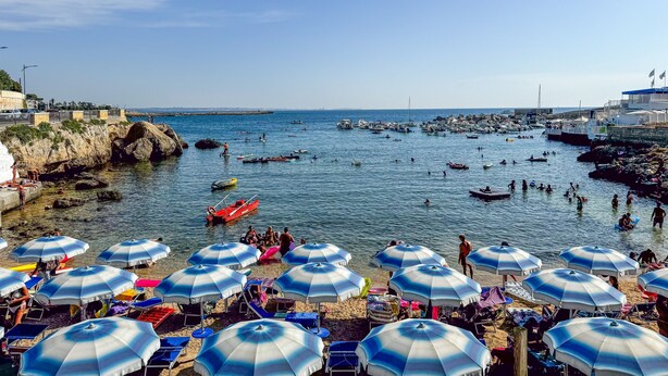 Une scène de plage côtière avec des parasols, des bateaux et des gens.