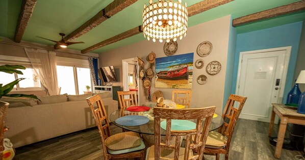 Un espace repas comprenant une table ronde en verre, des chaises en bois et un ventilateur de plafond.
