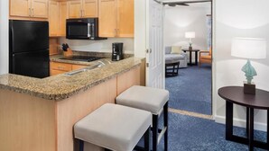 A compact kitchen with wooden cabinets, a black refrigerator, a microwave, and a granite countertop. There are two stools and a small table with a lamp. - Harborside 4 Atlantis Passes Included 1-23-27 - 1-30-27One Bedroom Villa 4 sleep (Paradise Island)