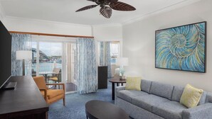 A hotel room with a sofa, armchair, and a desk. There is a large window with curtains, a ceiling fan, and a painting on the wall. - Harborside 4 Atlantis Passes Included 1-23-27 - 1-30-27One Bedroom Villa 4 sleep (Paradise Island)