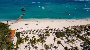 Una playa con un muelle que se adentra en el agua, palmeras y varios barcos.