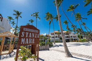 A wooden sign with 'STANZA MARE' written on it, palm trees, and a building in the background.
