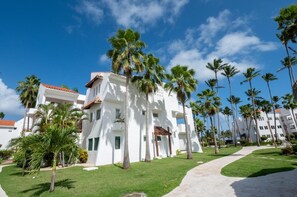 A white building with a red-tiled roof, surrounded by palm trees and a clear blue sky.