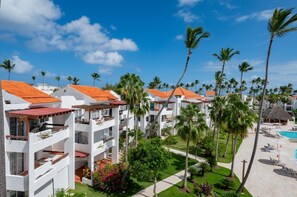 A resort with multiple white buildings, palm trees, a swimming pool, and a well-maintained lawn.