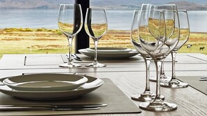 A table set with plates, cutlery, and wine glasses, overlooking a scenic landscape with mountains and a body of water. - Calmdale (Achnasheen)