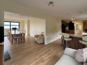 A modern kitchen with a dining area, a sofa, and a view through the glass door. - Calmdale (Achnasheen)