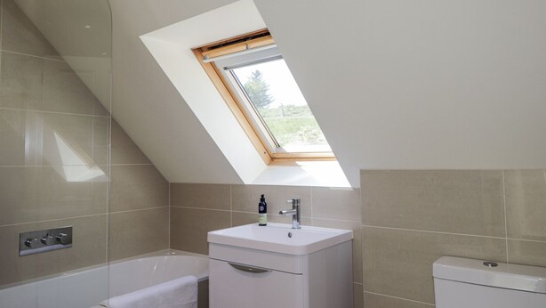 A modern bathroom with a skylight, a bathtub, a toilet, and a vanity with a sink. - Calmdale (Achnasheen)