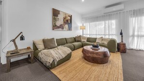 Ein modernes Wohnzimmer mit einer Eckcouch, einem runden Couchtisch, einer Lampe und einem Gemälde an der Wand.