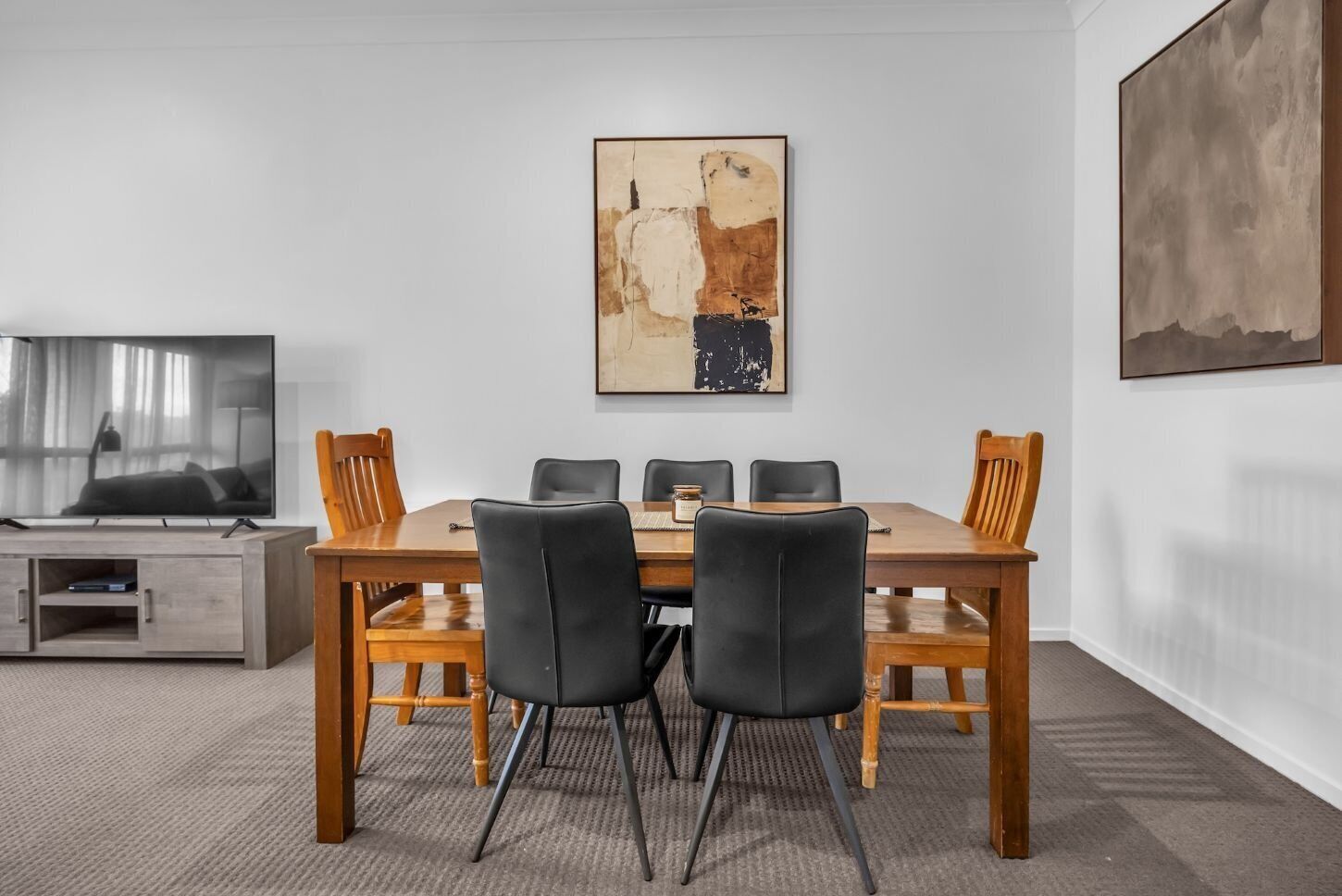 Un comedor con una mesa de madera, sillas negras y un cuadro en la pared.