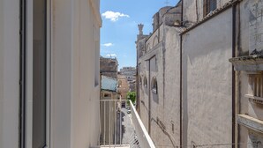 A narrow street with buildings on either side, a balcony with a railing, and a clear sky. - Apartment 'Ognissanti' with Private Terrace, Wi-Fi and Air Conditioning (Ragusa)