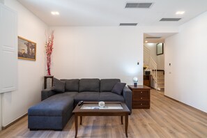 A living room with a sectional sofa, a coffee table, a small side table, and a staircase in the background.