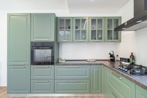 A kitchen with green cabinets, a built-in oven, a coffee maker, and a bottle of olive oil on the counter.