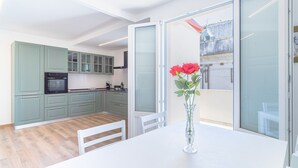 A modern kitchen with green cabinets, a white dining table, and a vase with red flowers. - Apartment 'Ognissanti' with Private Terrace, Wi-Fi and Air Conditioning (Ragusa)