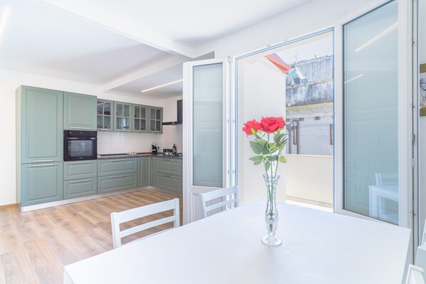 A modern kitchen with green cabinets, a white dining table, and a vase with red flowers.