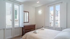 A bedroom with a bed, a dresser, a mirror, and a window with a view of buildings. - Apartment 'Ognissanti' with Private Terrace, Wi-Fi and Air Conditioning (Ragusa)