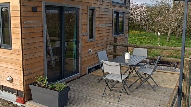 A modern wooden house with a deck, outdoor seating, and a pergola.