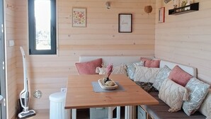 A cozy cabin interior with a wooden ceiling, a dining table, a bench with cushions, and a patterned rug.