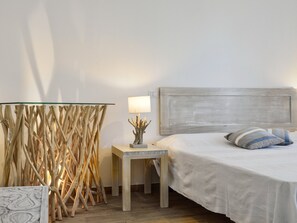 A bedroom with a bed, a bedside table with a lamp, and a wall-mounted shelf. - Villa 'Bua' with Private Pool, Wi-Fi, and Air Conditioning (Costa Rei)