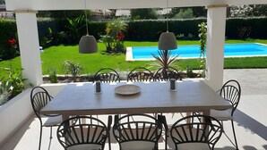 Portico coperto con tavolo e sedie, una lampada a sospensione e vista su una piscina.