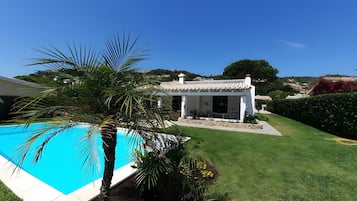 Ein Pool, ein weißes Gebäude mit einem Ziegeldach und eine gepflegte Rasenfläche.
