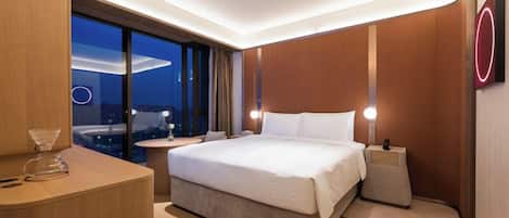 A modern hotel room with a large bed, bedside tables, a view of the cityscape, and a circular light fixture on the wall.