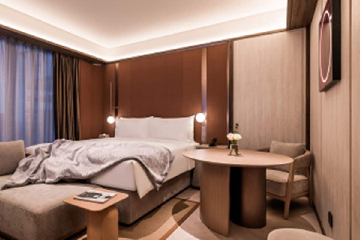 A modern hotel room with a large bed, a small round table, a sofa, and a desk.