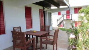 An outdoor patio with a wooden table and chairs, a small plant, and a staircase leading to an upper level.