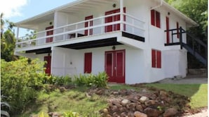 A two-story house with a balcony, red shutters, and a stone foundation.