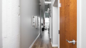 A hallway with a wooden door on the right, a white wall on the left, and a view into a room with a white chair and a small table. - Cozy, Modern Bay Views for Six! (Sandusky)