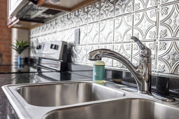 A kitchen with stainless steel sinks, a modern faucet, and decorative backsplash tiles. - Cozy, Modern Bay Views for Six! (Sandusky)