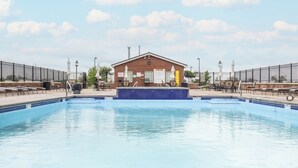 A swimming pool with lounge chairs and umbrellas, a brick building with a sign, and a fenced area. - Cozy, Modern Bay Views for Six! (Sandusky)