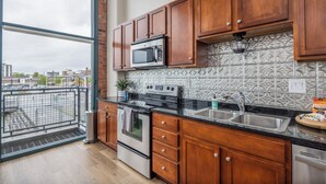 A modern kitchen with wooden cabinets, a stainless steel sink, and a large window overlooking a cityscape. - Cozy, Modern Bay Views for Six! (Sandusky)