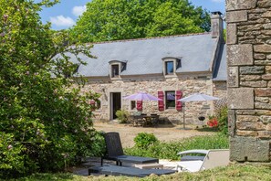 A stone building with a sloped roof, outdoor seating with umbrellas, and a garden area.