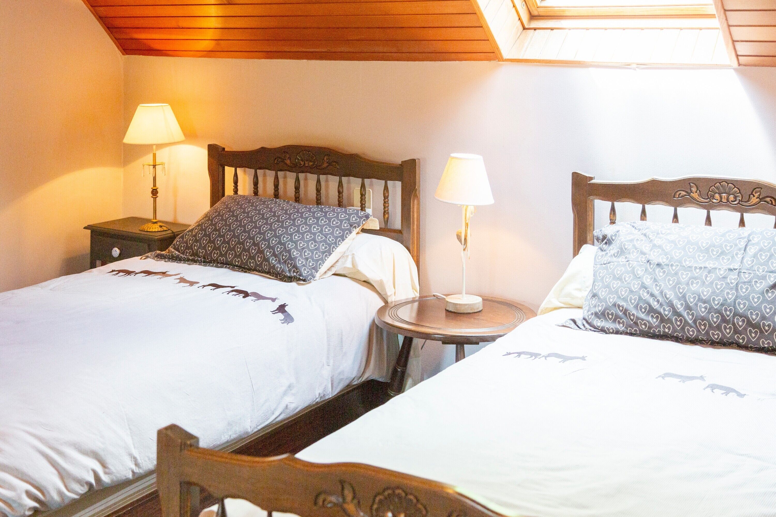 Une chambre avec deux lits, chacun doté d’une tête de lit, d’une table de chevet avec une lampe, et d’une petite table ronde placée entre les lits.