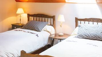 Une chambre avec deux lits, chacun doté d’une tête de lit, d’une table de chevet avec une lampe, et d’une petite table ronde placée entre les lits.