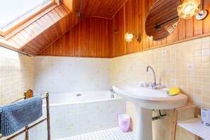 A bathroom with a wooden ceiling, a bathtub, a sink, and a mirror.