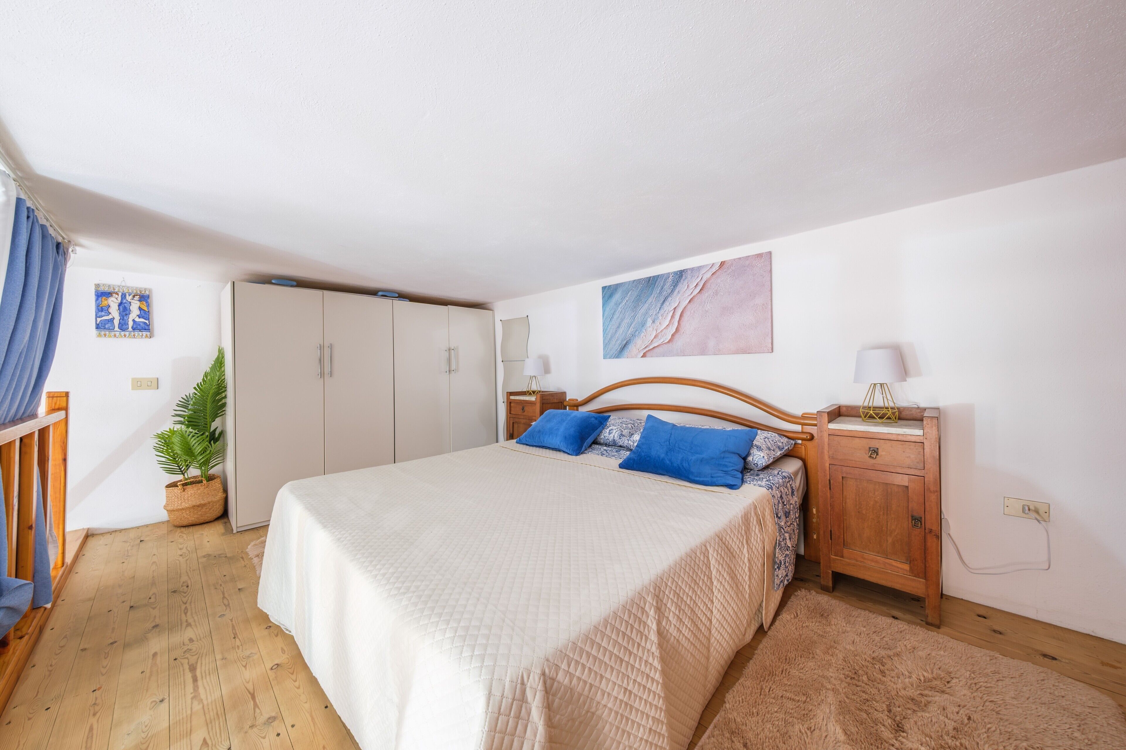 A bedroom with a bed, wooden headboard, bedside tables, a wardrobe, and a potted plant.