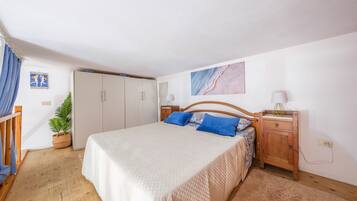 A bedroom with a bed, wooden headboard, bedside tables, a wardrobe, and a potted plant.